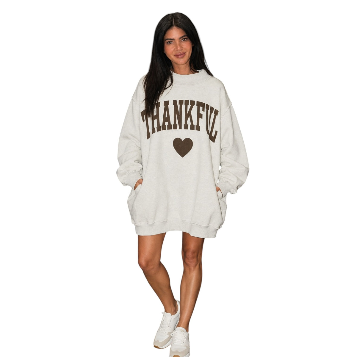 A woman modeling an oversized off-white sweatshirt with 'THANKFUL' and a heart printed in brown on the front, paired with white sneakers against a plain white background.