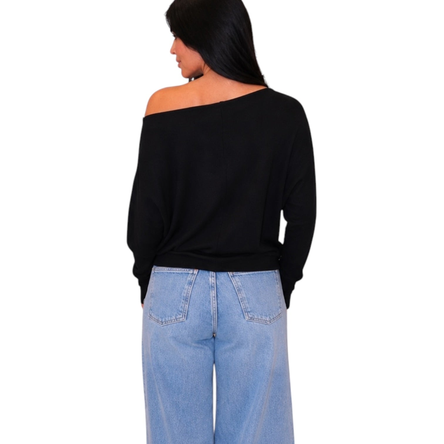 A woman shown from the back wearing a black off-the-shoulder long-sleeve top and light blue jeans against a plain white background.