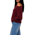 A woman wearing a dark red off-the-shoulder long-sleeve top and light blue jeans, shown from a side profile against a plain white background.