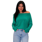 A woman modeling a bright green off-the-shoulder long-sleeve knit top with light-wash blue jeans, set against a plain white background.