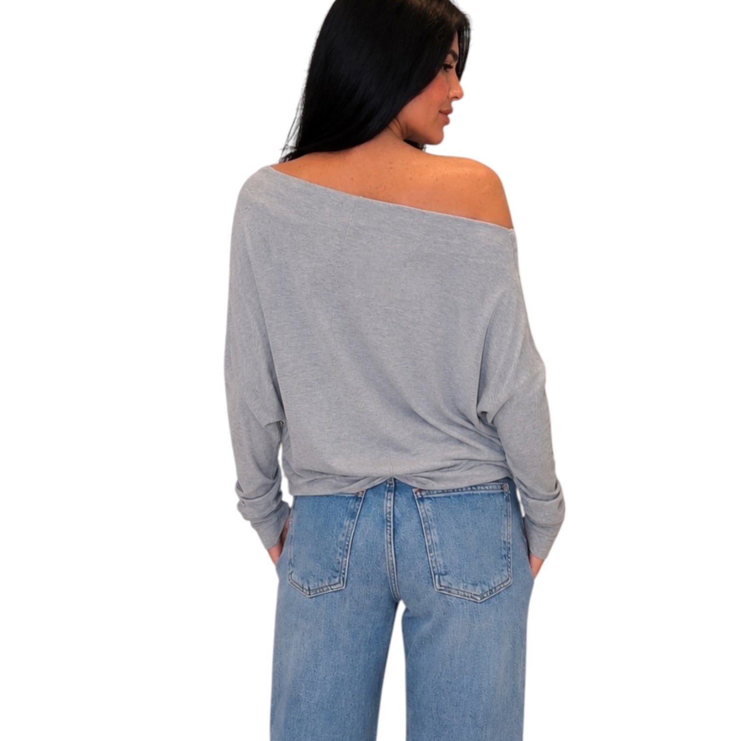 A woman shown from the back wearing a light gray off-the-shoulder long-sleeve top and light blue jeans against a plain white background.