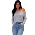 A woman modeling a light gray off-the-shoulder long-sleeve top with light-wash blue jeans against a plain white background.