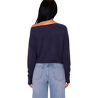 A woman shown from the back wearing a dark navy off-the-shoulder long-sleeve crop top and light blue jeans against a plain white background.