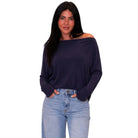 A woman modeling a dark navy off-the-shoulder long-sleeve top paired with light blue jeans, set against a plain white background.