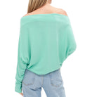 Woman wearing a light green off-shoulder top and blue jeans on a white background