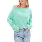 Woman wearing a light green off-shoulder sweater and blue jeans on a white background