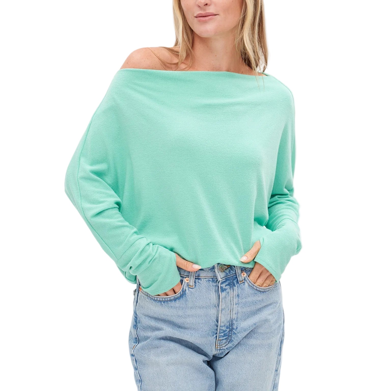 Woman wearing a light green off-shoulder sweater and blue jeans on a white background
