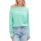 Person wearing a light green off-shoulder top and blue jeans on a white background