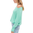 Woman wearing a light green off-shoulder top and blue jeans on a white background