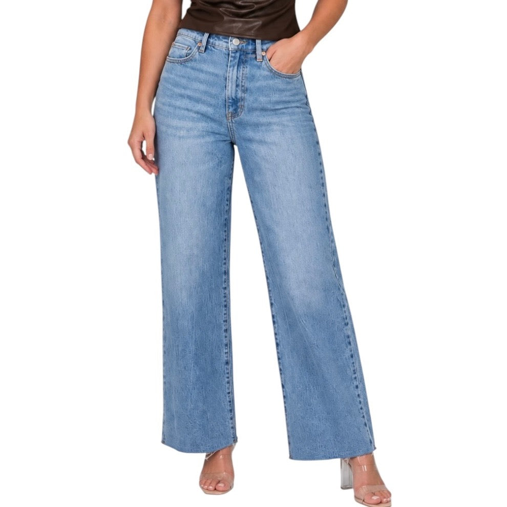 A model wearing a pair of light blue wide-leg denim jeans, paired with a dark brown top and clear high-heeled sandals, shown against a plain white background.