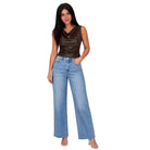 A woman modeling a pair of wide-leg light blue denim jeans with a brown satin sleeveless top, standing against a solid white background.
