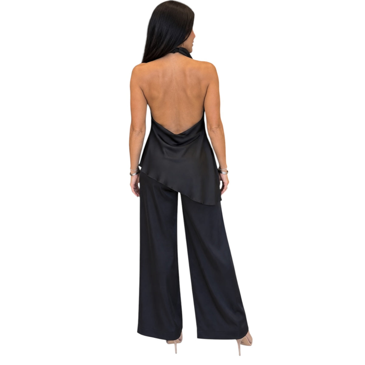 A woman shown from the back wearing a black satin-like open-back jumpsuit with wide legs and nude heels, against a plain white background.