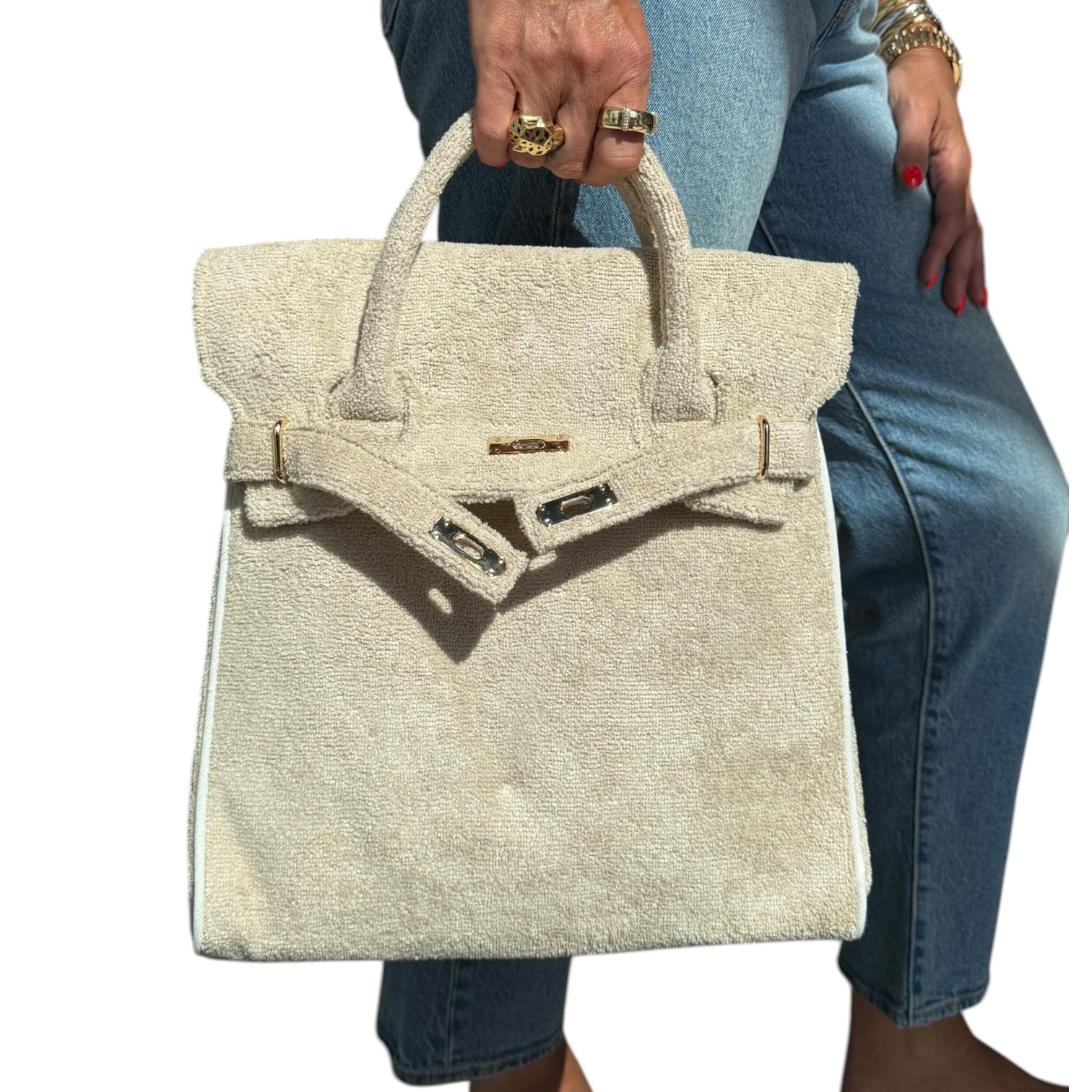 Beige textured handbag held by a person wearing jeans and gold rings.
