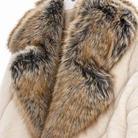 Close-up of a plush cream-colored coat with a large, luxurious shaggy faux-fur collar in mixed brown, gray, and black tones.