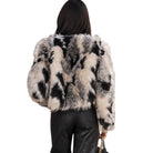 A woman shown from the back wearing a cropped faux fur jacket with a black, gray, and beige mottled pattern, paired with black leather pants against a plain white background.
