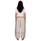 A woman viewed from behind wearing loose, wide-leg beige pants with a white t-shirt and brown sandals, set against a plain white background.