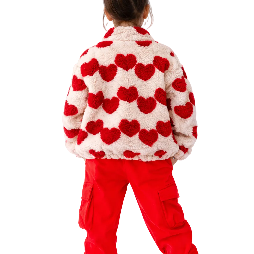 Person wearing a heart-patterned sweater and red pants with a white background
