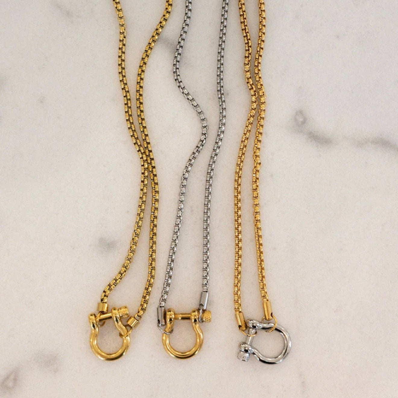 Three gold and silver chain necklaces on a marble surface