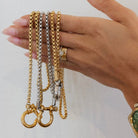 Hand holding three gold chains against a white background