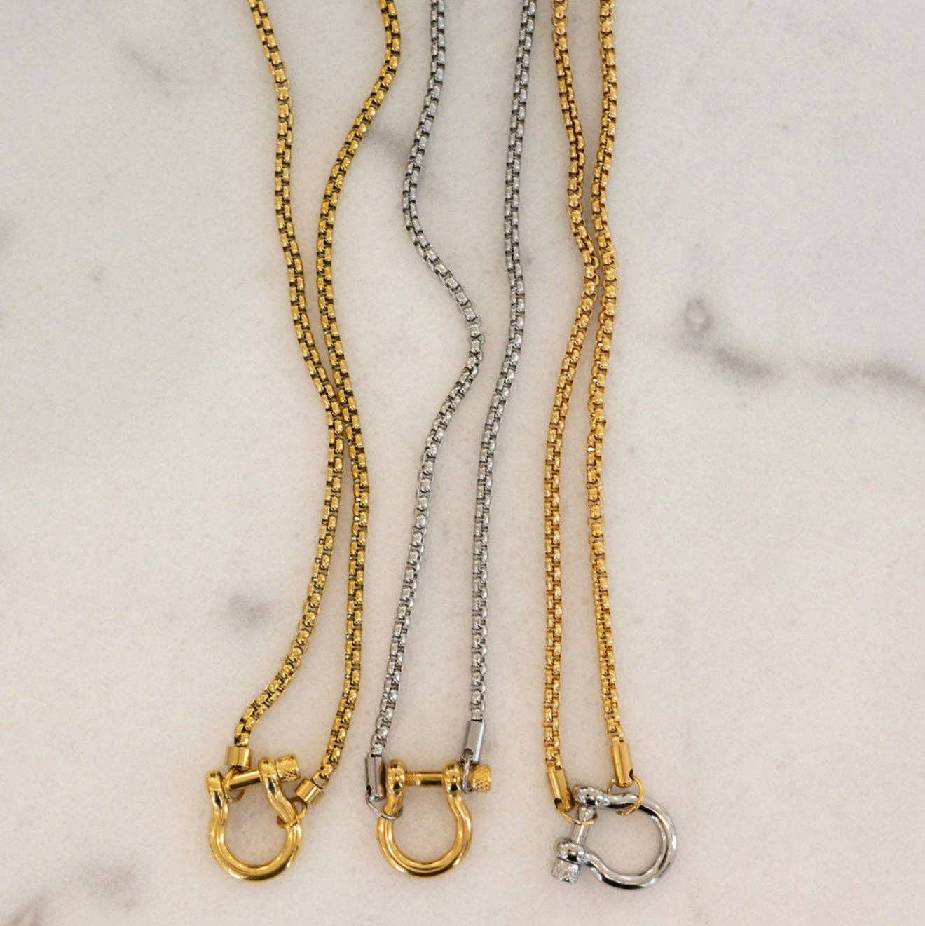 Three gold and silver chain collars on a marble surface