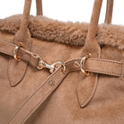 Close-up of a brown suede handbag with gold hardware on a white background