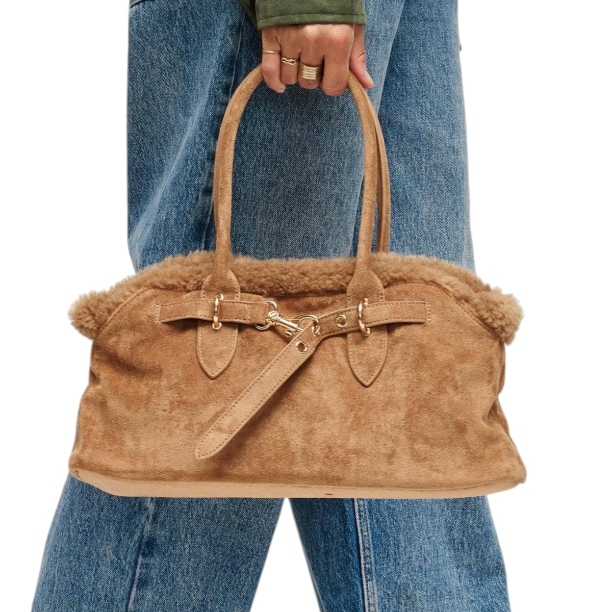 A tan suede handbag with a fluffy shearling-style lining and double top handles, held by a person wearing blue jeans against a plain white background.
