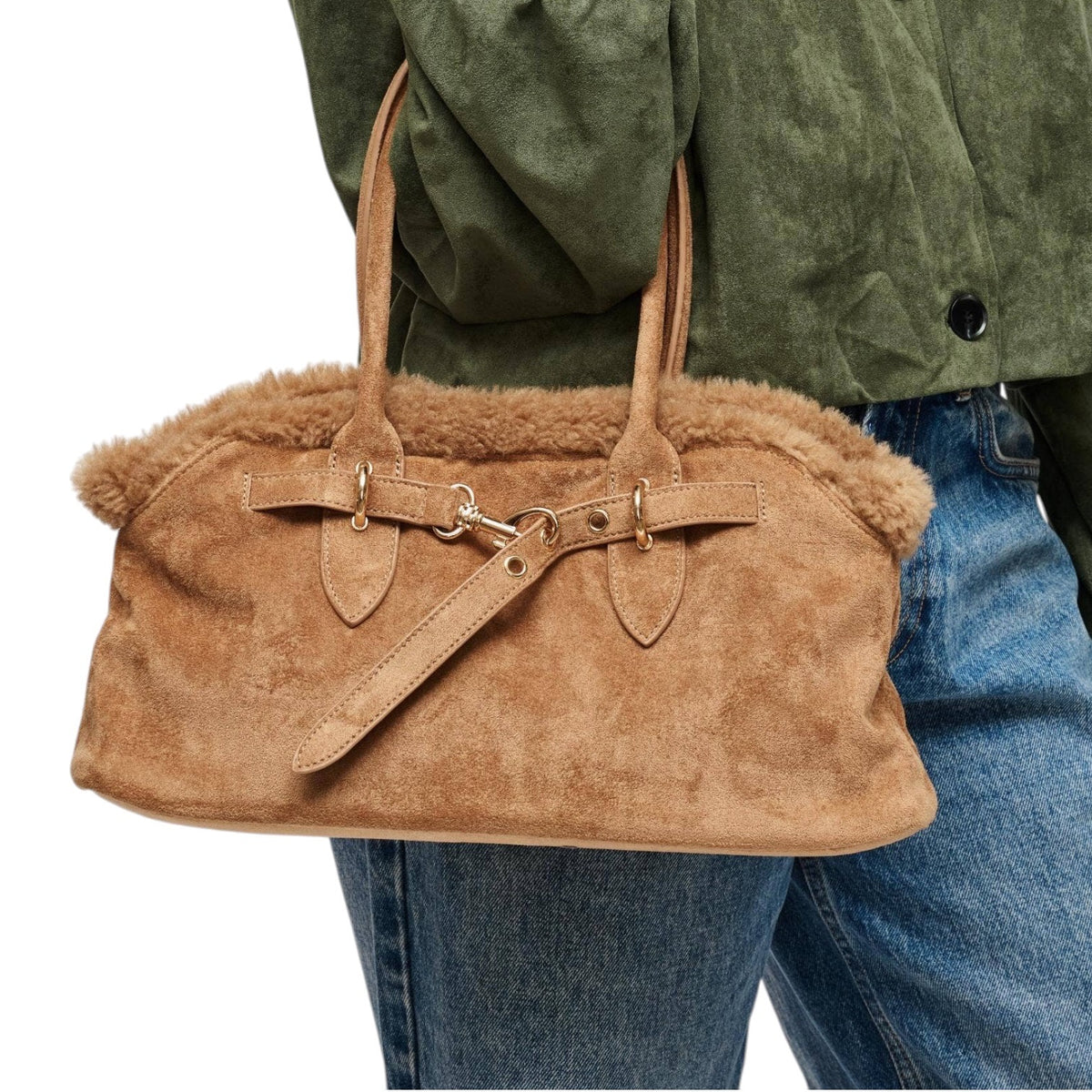 A tan suede handbag with a fluffy shearling-style lining and double shoulder straps, shown being carried over the shoulder of a person wearing an olive green jacket and blue jeans against a white background.