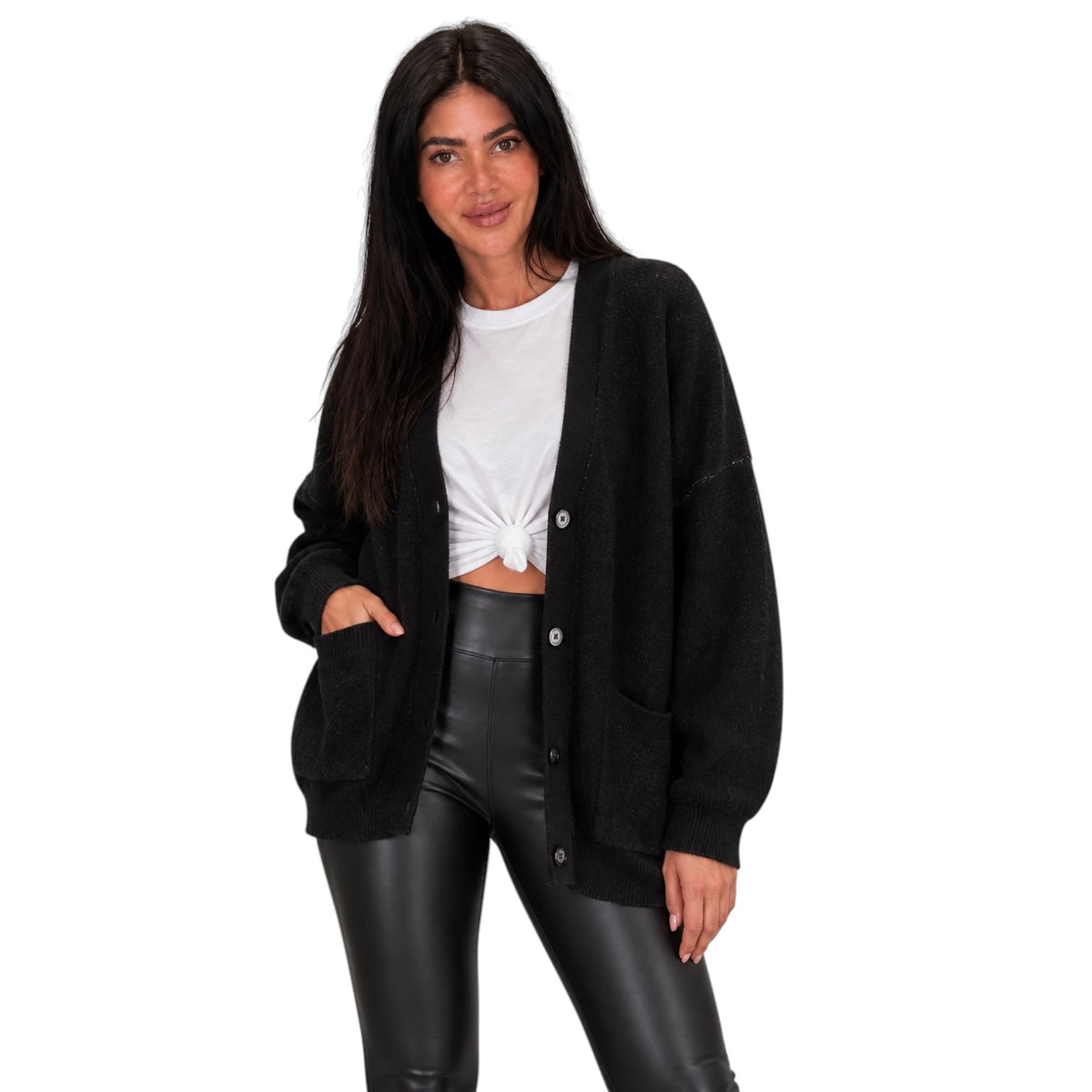 A woman modeling a black knit button-up cardigan over a white cropped tie-front t-shirt and black faux-leather pants, photographed against a plain white studio background.