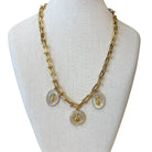 A gold-tone chain necklace displayed on a cream fabric mannequin bust. The necklace features three oval pendants with white inlay and gold religious-style portraits.