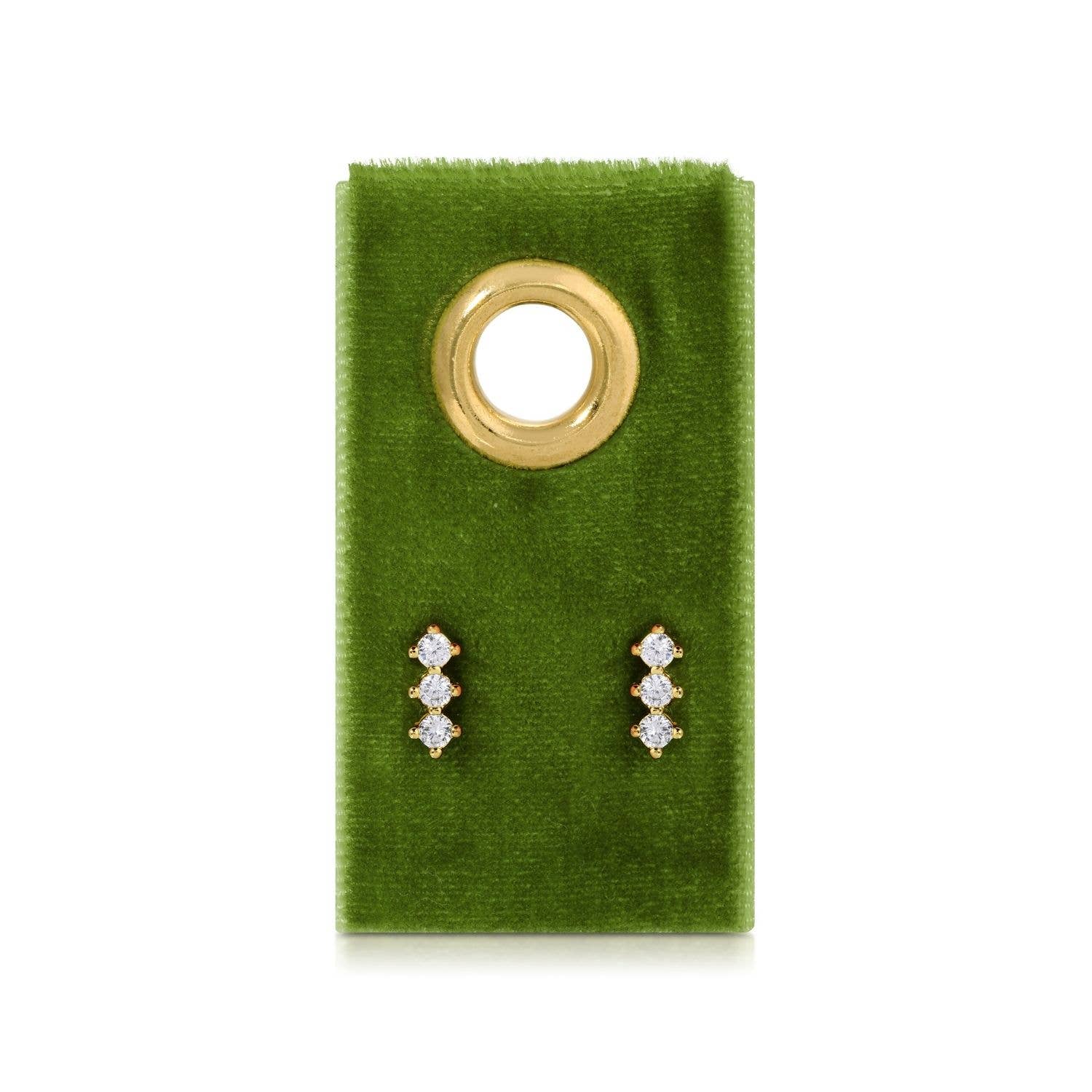Pair of diamond stud earrings on a green velvet card with a gold ring.