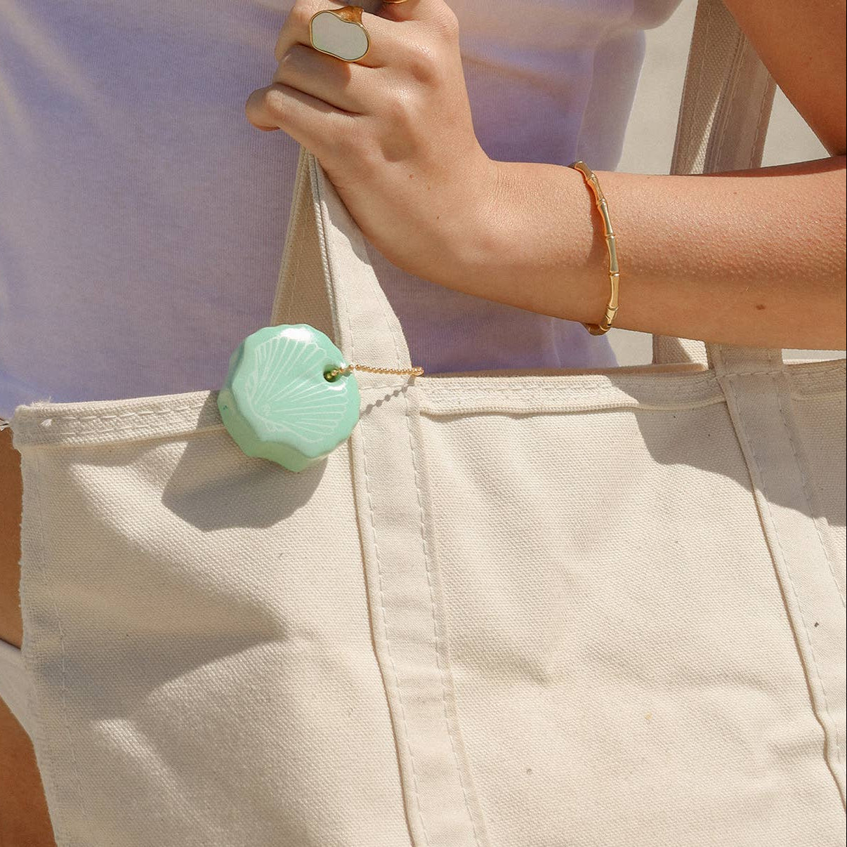 Person wearing a white top with a shell design and beige pants, holding a light green bag.