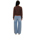 A woman viewed from behind wearing a brown long-sleeve cropped sweatshirt and light-wash wide-leg denim jeans against a plain white background.