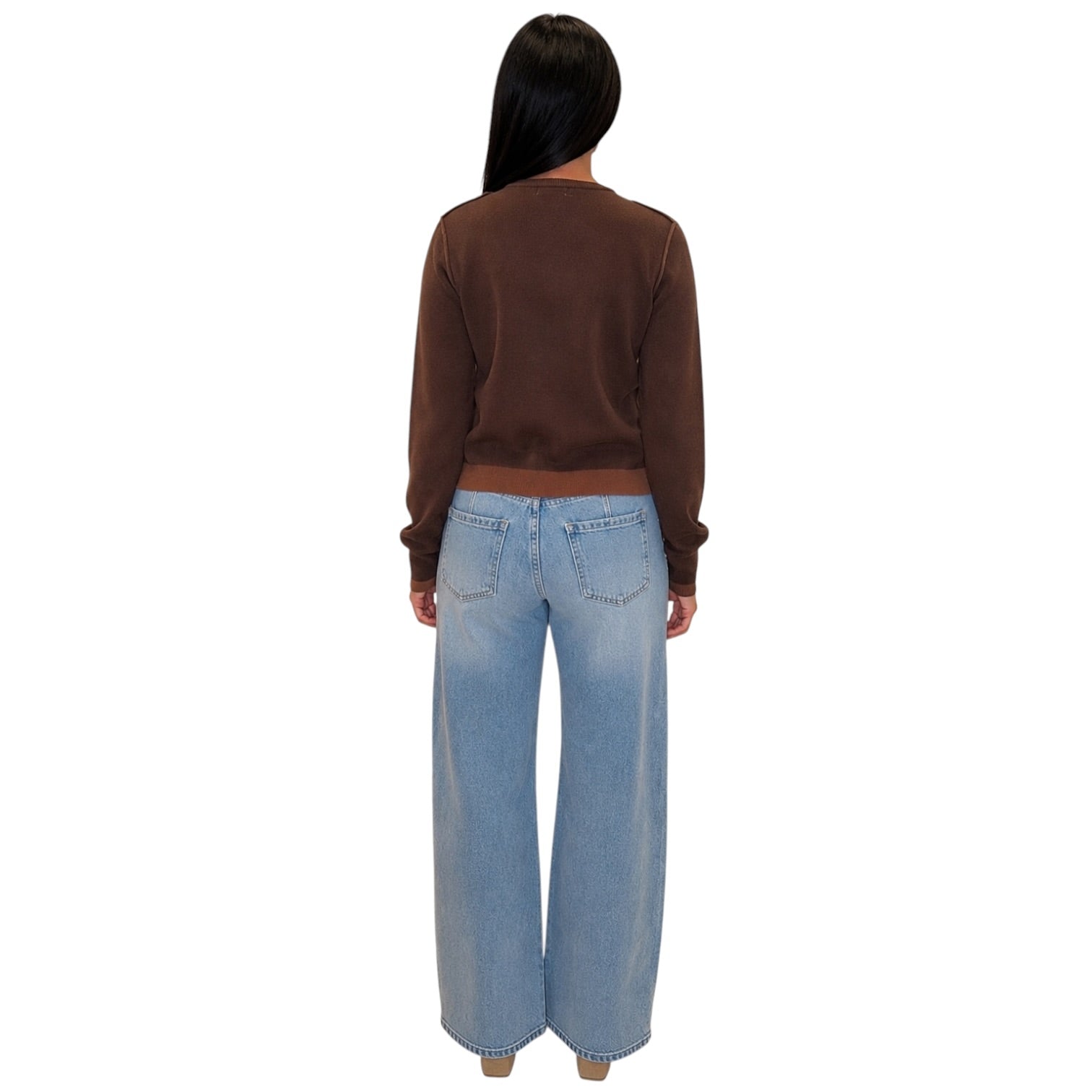A woman viewed from behind wearing a brown long-sleeve cropped sweatshirt and light-wash wide-leg denim jeans against a plain white background.