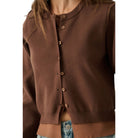 A close-up of a person wearing a brown knit cardigan with a button front, shown from the shoulders to the waist against a plain white background.
