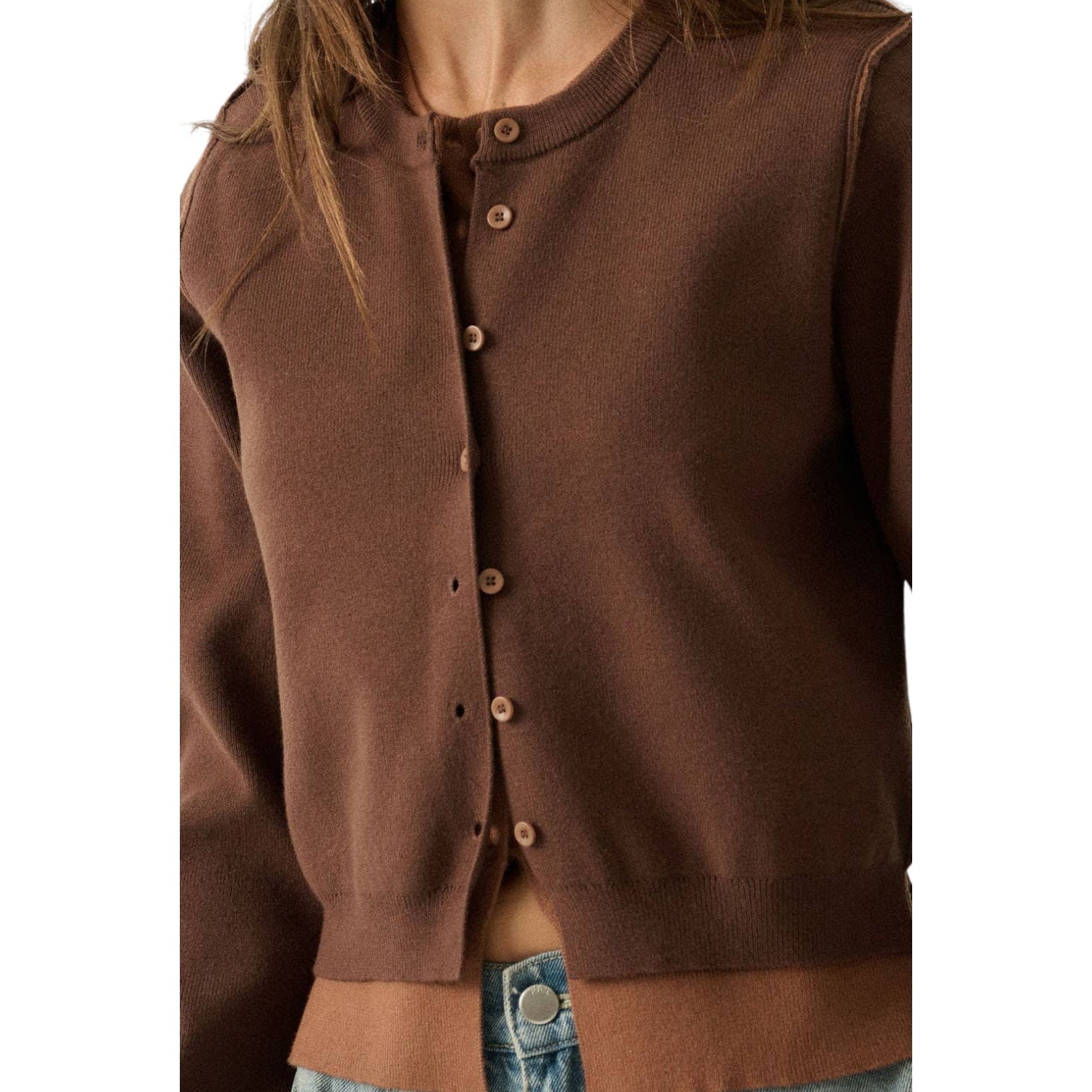 A close-up of a person wearing a brown knit cardigan with a button front, shown from the shoulders to the waist against a plain white background.