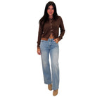 A woman modeling a brown button-front knit cardigan with light-wash blue jeans and tan boots, shown against a plain white background.
