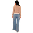 A woman shown from the back wearing a light beige long-sleeve knit top and light blue wide-leg jeans, set against a plain white background.
