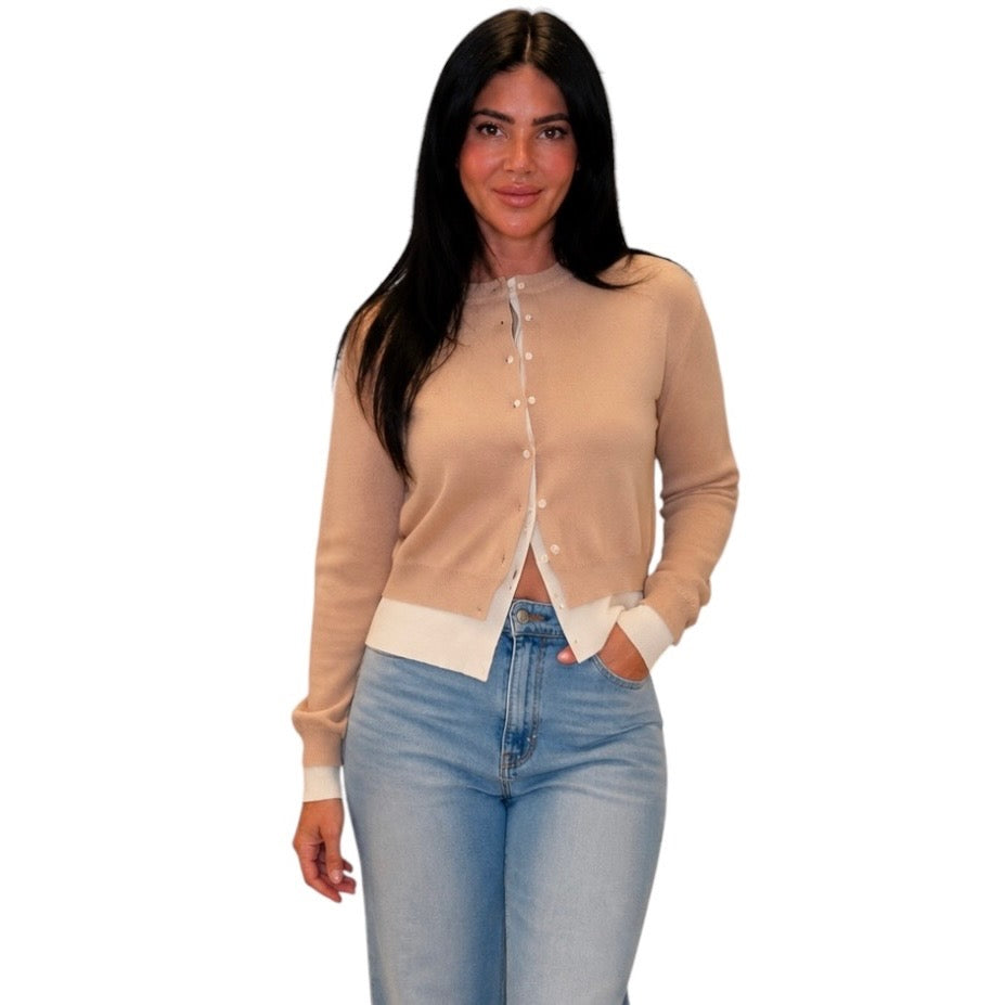 A woman modeling a beige long-sleeve knit cardigan with white trim and buttons, paired with light blue jeans, against a plain white background.