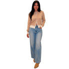 A woman modeling a beige cardigan with white trim and light-wash wide-leg jeans, standing against a plain white background.