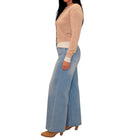 A woman shown from the side wearing a light taupe cardigan, light-wash wide-leg blue jeans, and tan heeled shoes against a plain white background.