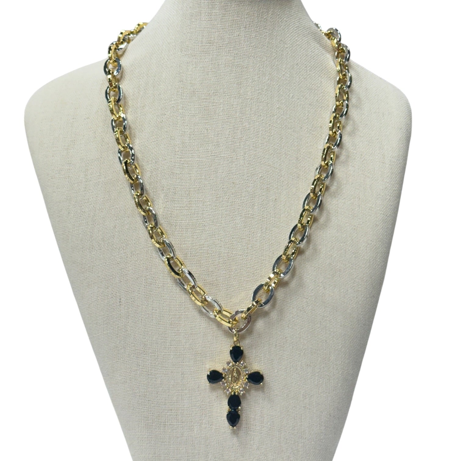 A gold and silver chain necklace with a cross pendant featuring black stones, displayed on a beige fabric mannequin bust against a white background.