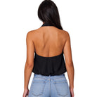A woman shown from the back wearing a black halter-style sleeveless top with a draped open back, paired with light blue jeans, against a plain white background.