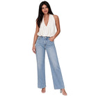 A woman modeling a white sleeveless halter top and light-wash wide-leg blue jeans against a plain white background.
