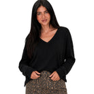 A woman modeling a black long-sleeve V-neck top with raw, frayed edges, paired with leopard-print pants, against a solid white background.