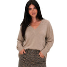 A woman modeling a beige v-neck knit sweater with long sleeves, paired with leopard-print pants, against a plain white background.
