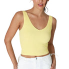 Woman wearing a yellow tank top and white pants on a white background