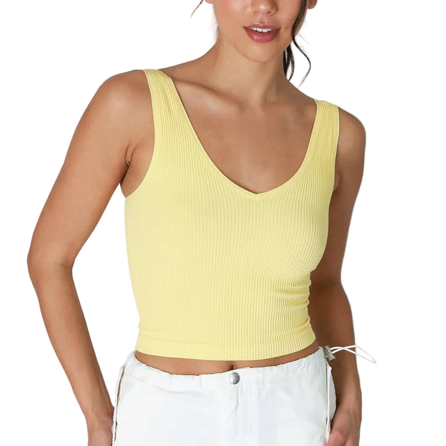 Woman wearing a yellow tank top and white pants on a white background