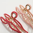 Two hair clips, one red and one pink, with gold hardware on a white background.