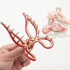 Red and gold butterfly hair clip held by a hand on a white background