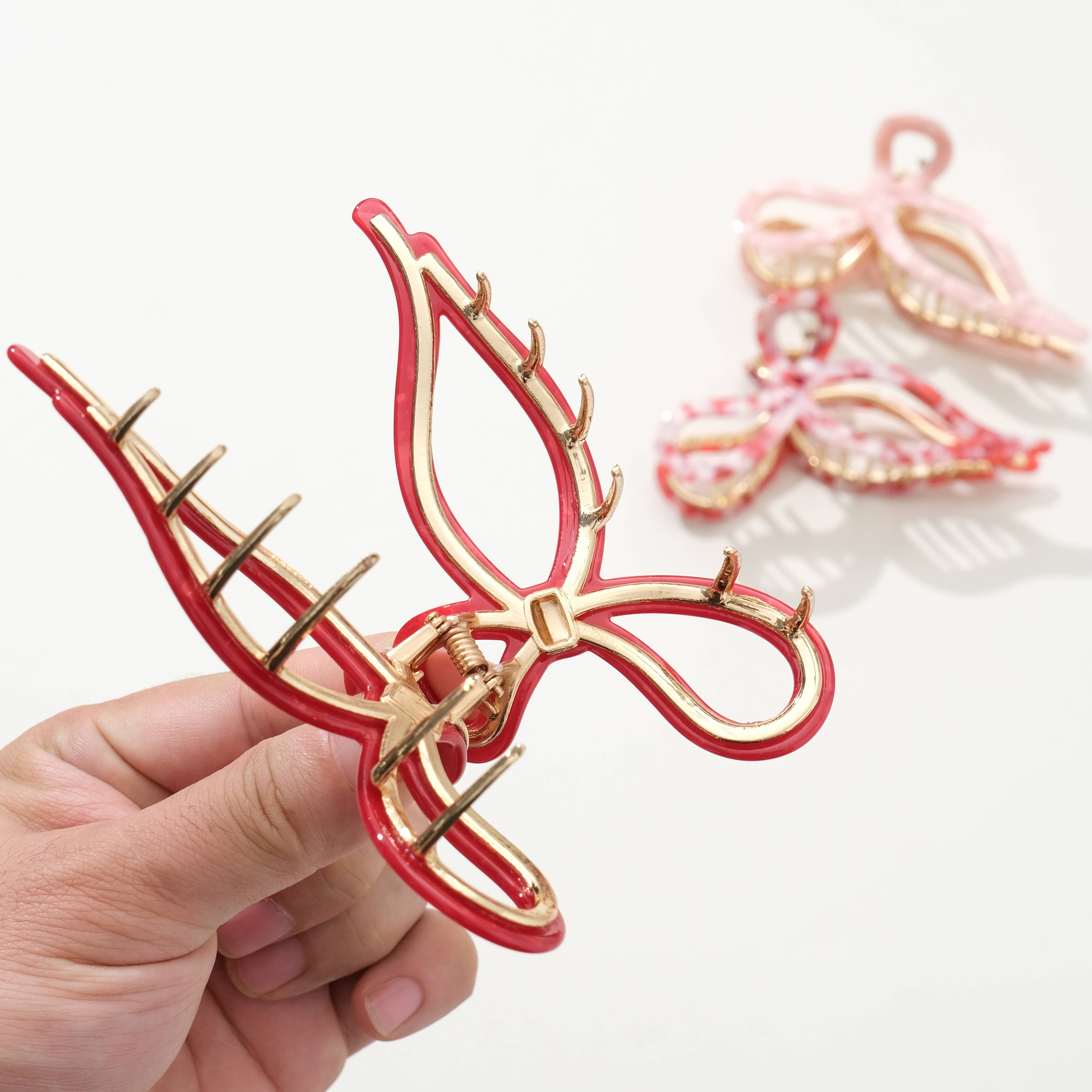 Red and gold butterfly hair clip held by a hand on a white background
